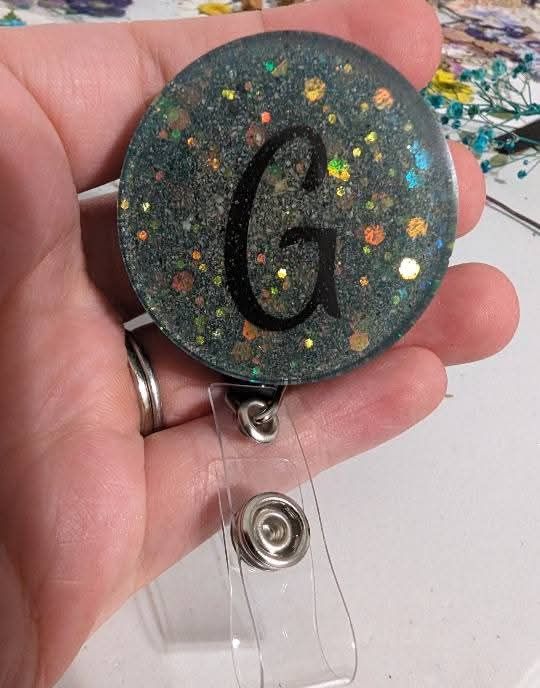 black glitter badge-reel with a G in the middle 